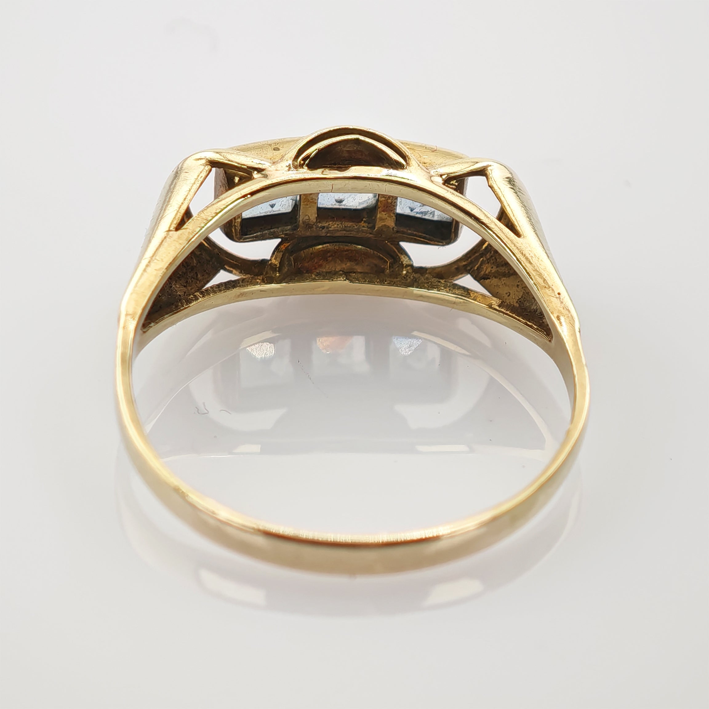 Seitliche Ansicht eines Goldrings mit einem blauen Edelstein in dreieckiger Fassung auf weißem Seitliche Ansicht eines Goldrings mit sichtbarem Ringband und Edelsteinfassung.