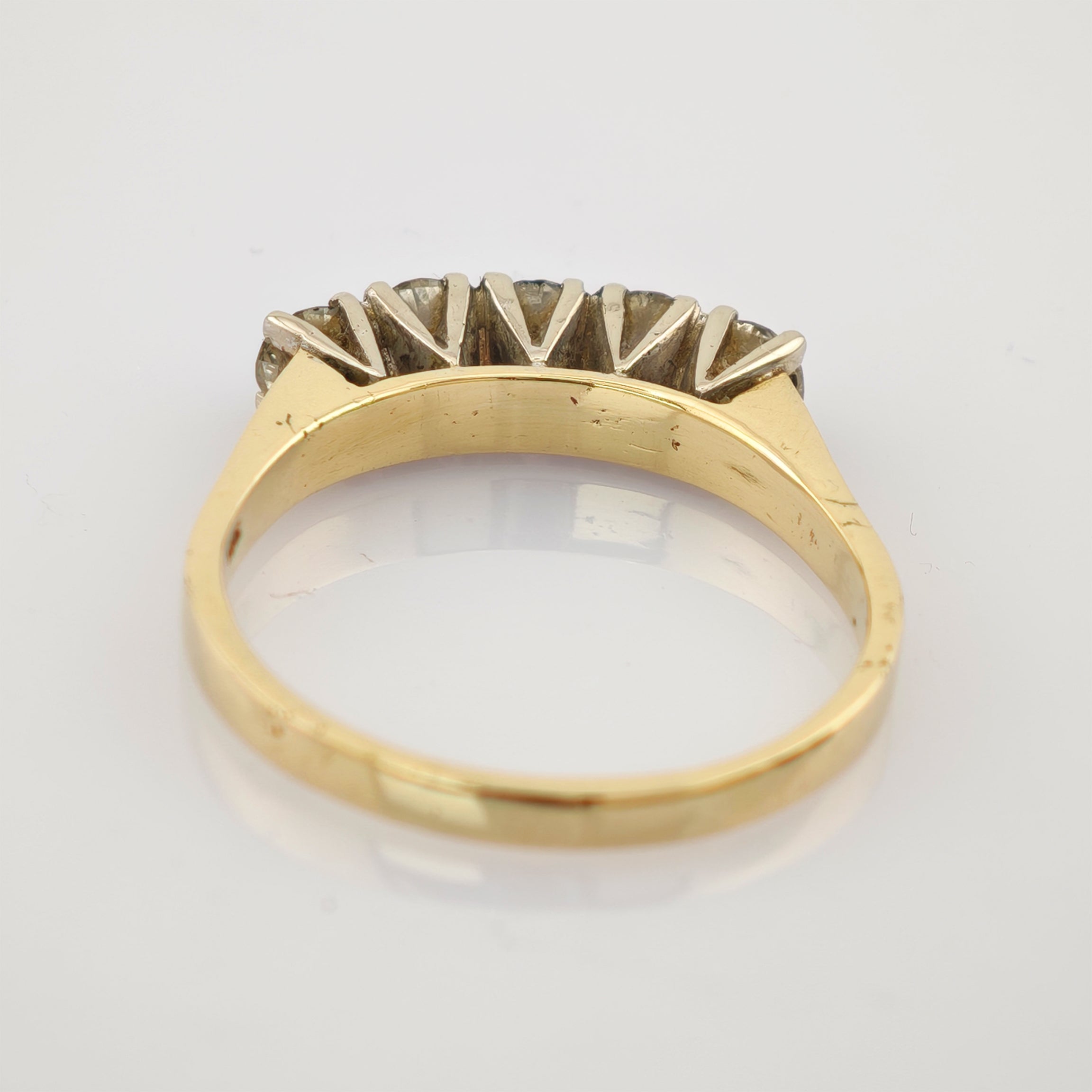 Seitliche Ansicht eines Goldrings mit fünf Diamanten, gehalten von silbernen Krappen, auf weißem Untergrund.