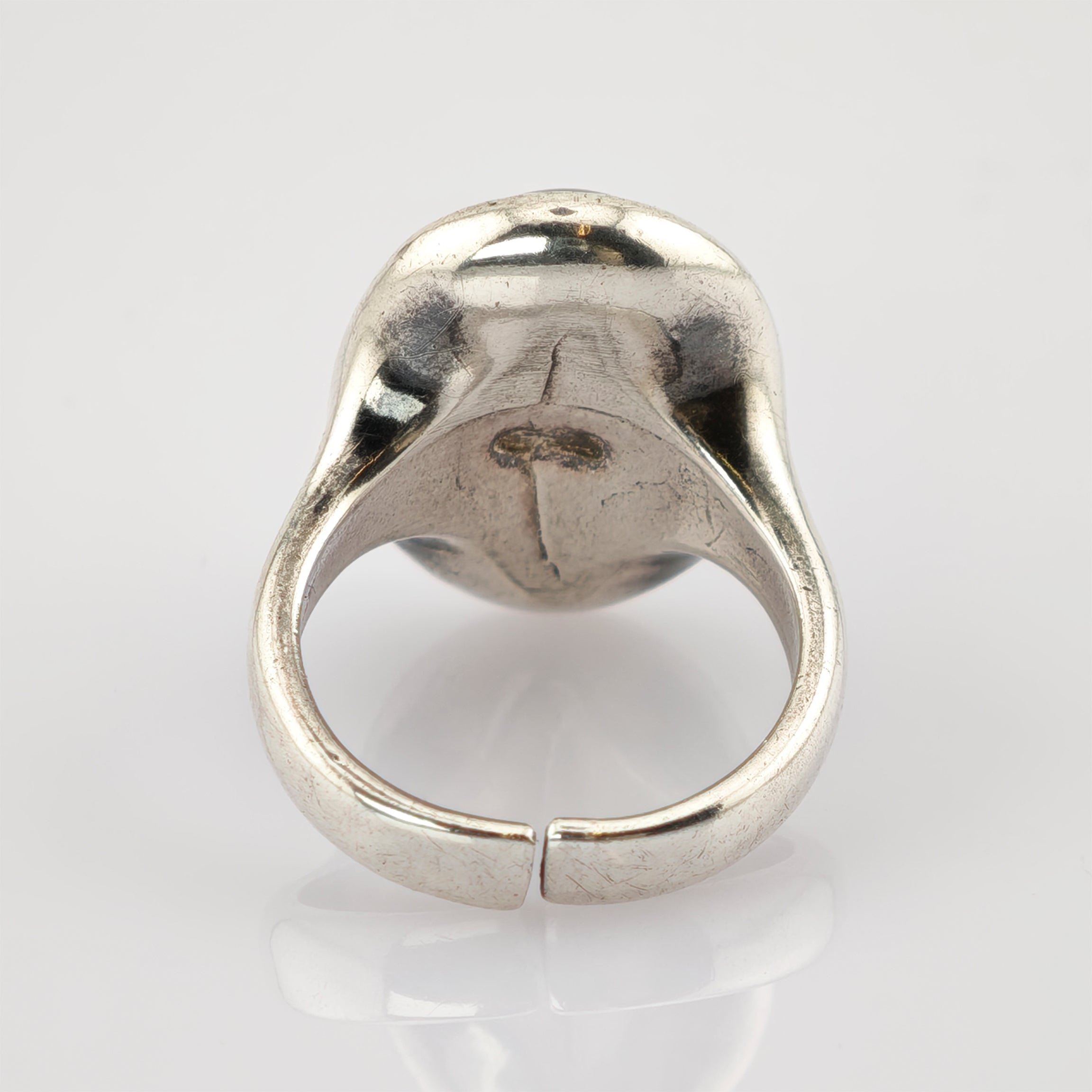 Silberfarbener Metallring mit offenem, verstellbarem Band und sichtbaren Gebrauchsspuren vor weißem Hintergrund.