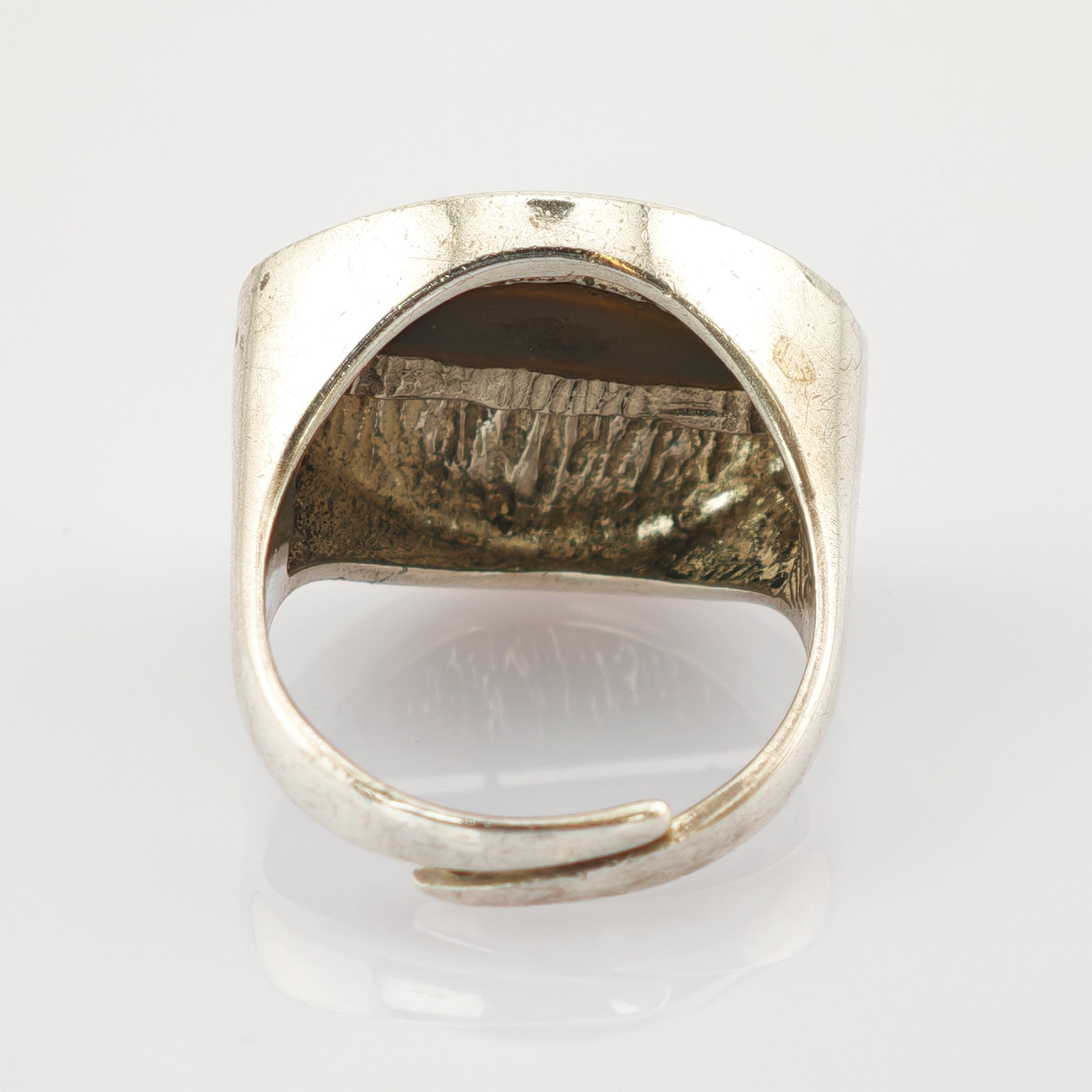 Silberfarbener verstellbarer Ring mit offenem Band und texturierter Innenseite vor weißem Hintergrund.