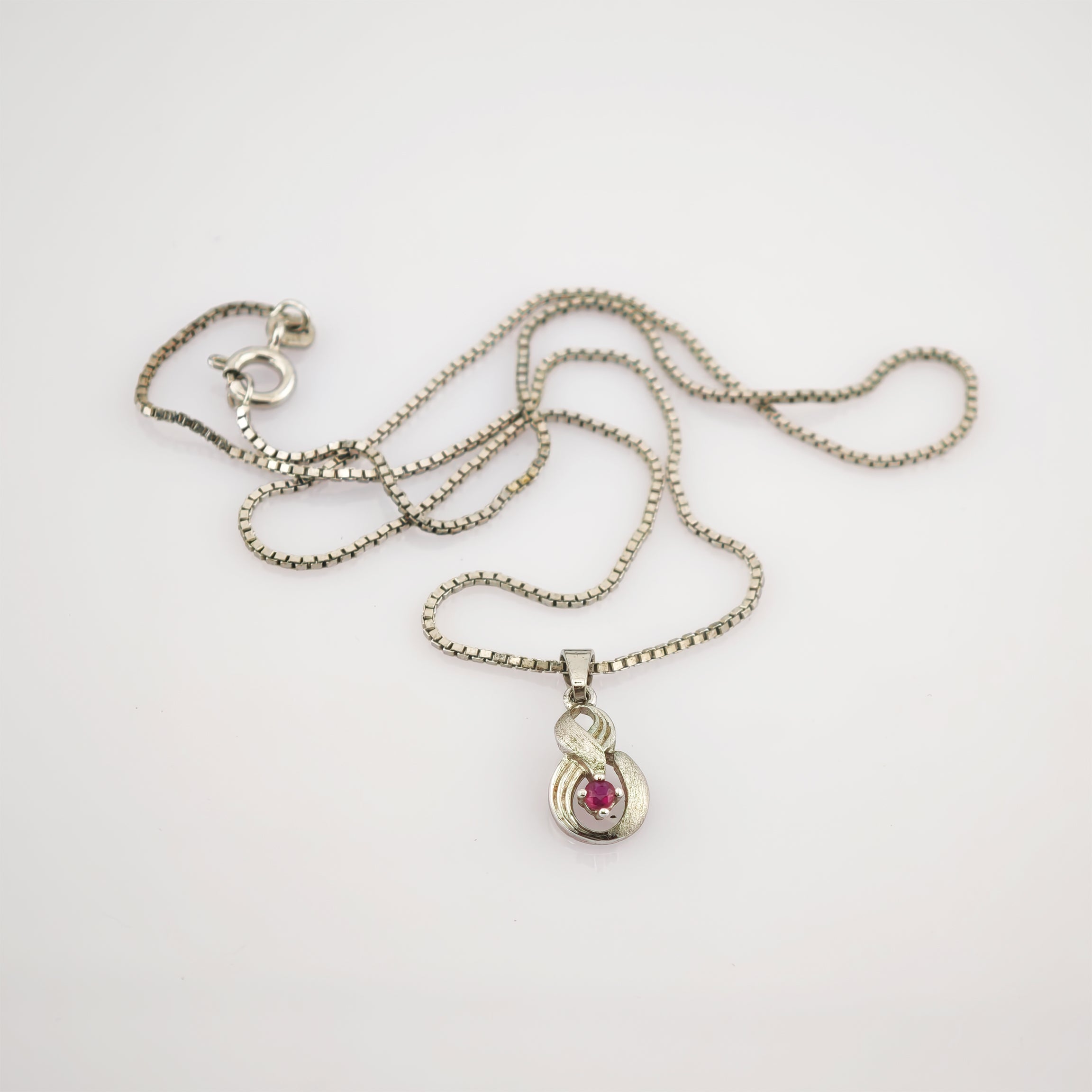 Silberne Halskette mit Kastenkettenmuster und geschwungenem Anhänger mit rotem Rubin.