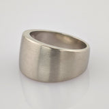 Silberner Ring mit asymmetrischem Design und matter Oberfläche auf reflektierender weißer Fläche.