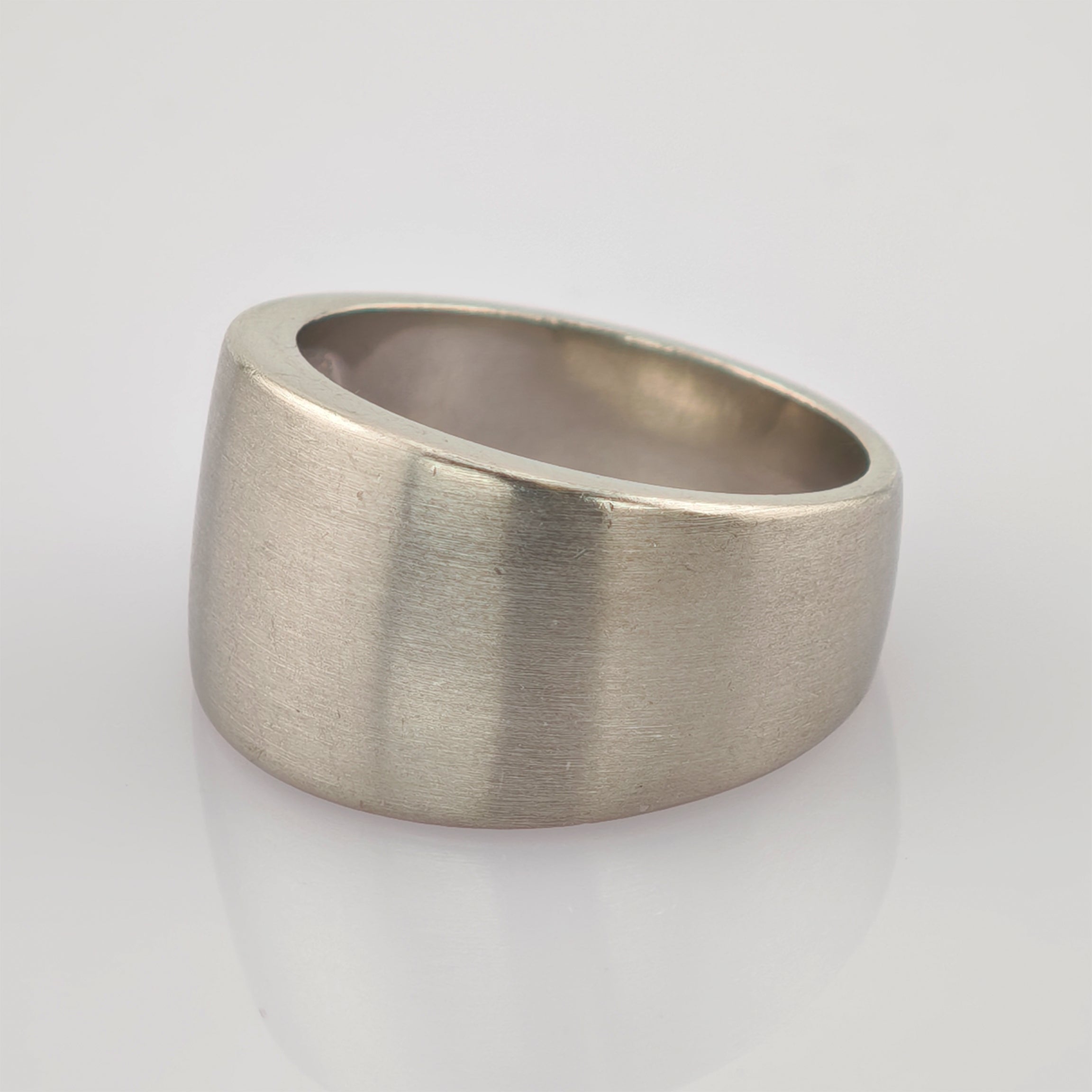 Silberner Ring mit asymmetrischem Design und matter Oberfläche auf reflektierender weißer Fläche.