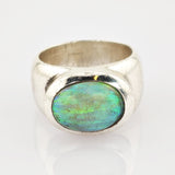 Nahaufnahme eines silbernen Rings mit ovalem blau-grünem Edelstein und breitem, abgenutztem Band.