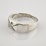 Silberner Ring mit breitem Band, kleinem Edelstein und diagonal gerilltem Design auf spiegelnder Oberfläche.