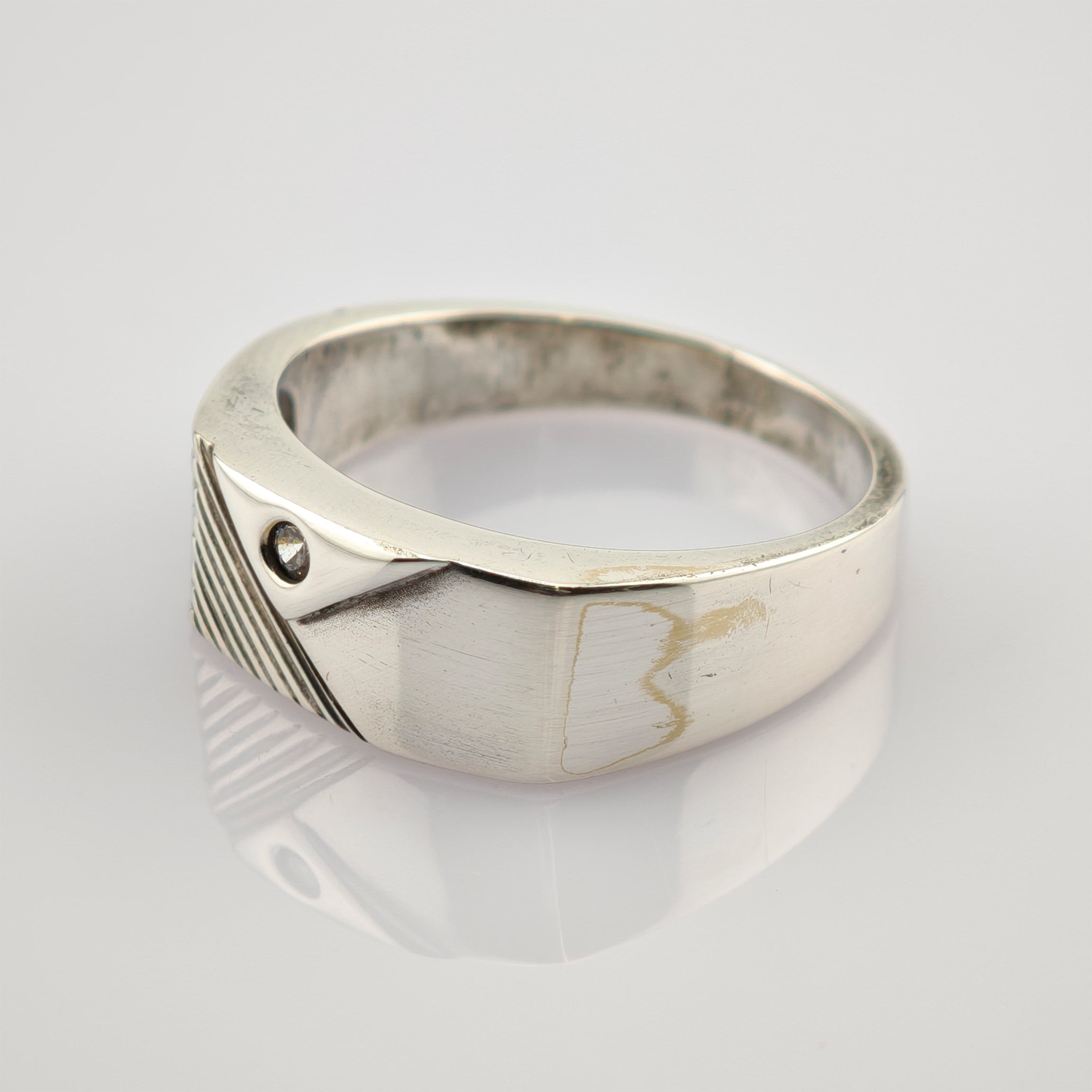 Silberner Ring mit breitem Band, kleinem Edelstein und diagonal gerilltem Design auf spiegelnder Oberfläche.