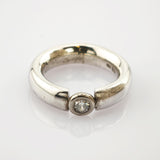 Silberner Ring mit breitem, offenem Band und einem runden Diamanten in Zargenfassung, minimalistisch und elegant.