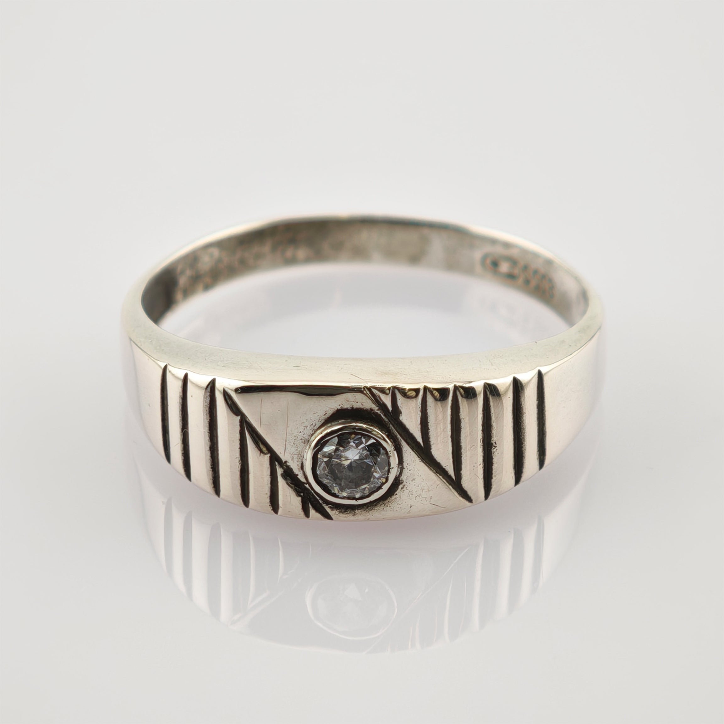 Silberner Ring mit diagonalen und vertikalen Gravuren und klarem Edelstein auf weißer Oberfläche