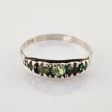 Silberner Ring mit fünf dunkelgrünen Steinen auf weißem reflektierendem Untergrund