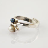Silberner Ring mit elegantem Design und zwei Perlen, schwarz und weiß, auf glänzender weißer Oberfläche.