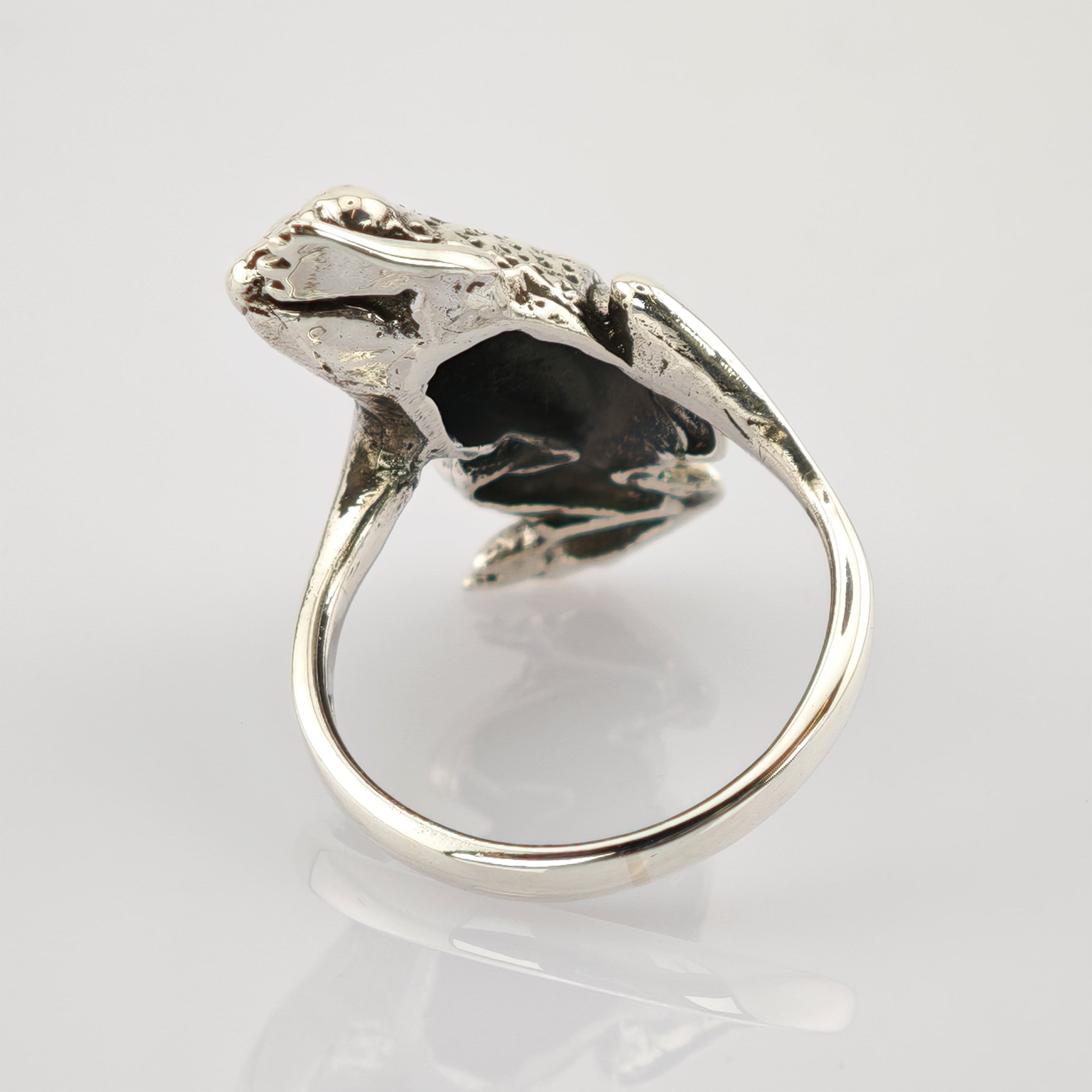 Silberner Ring in Form eines detaillierten Frosches mit realistischer Textur auf reflektierender Oberfläche.