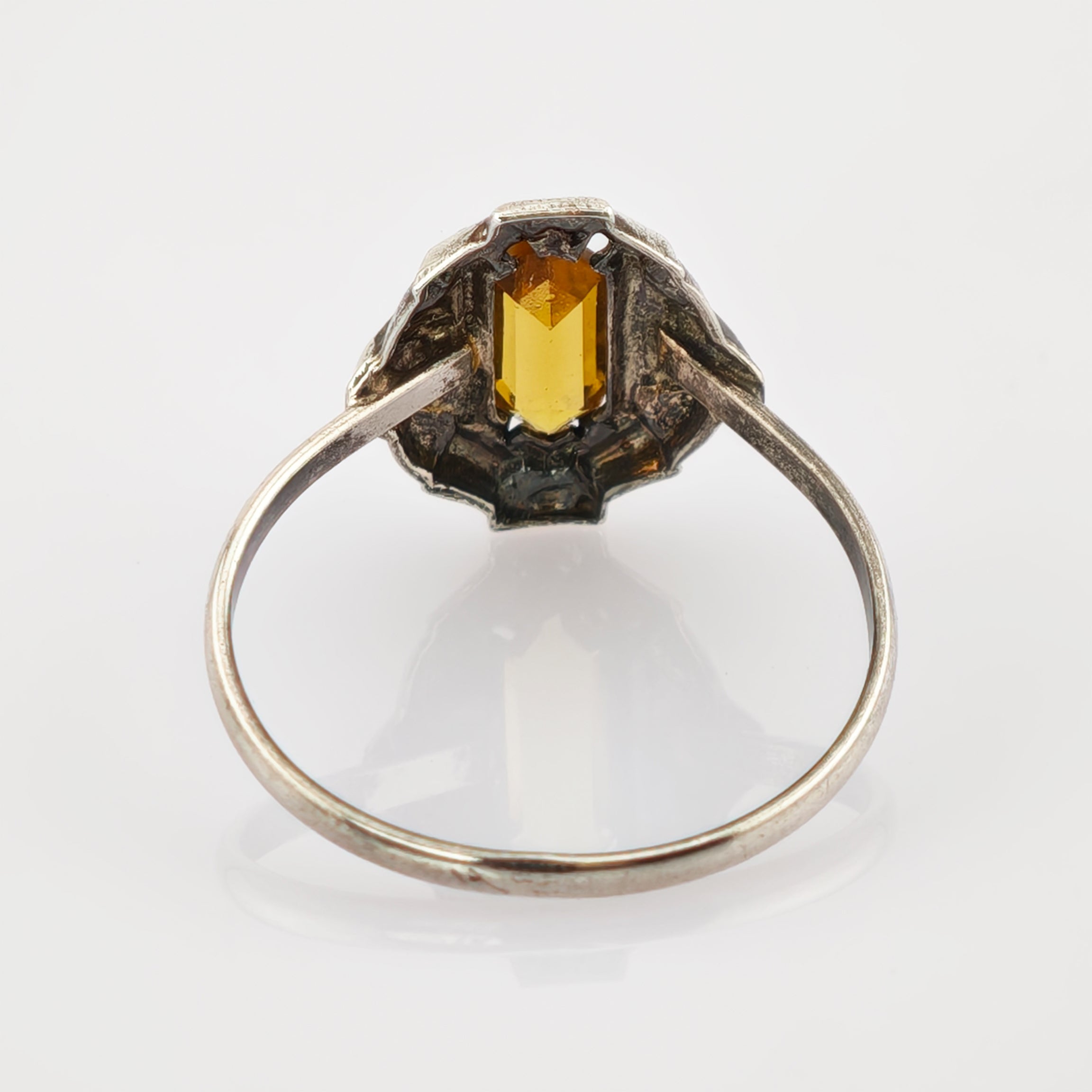 Silberner Ring mit rechteckigem gelbem Edelstein und verzierter Fassung auf reflektierender Oberfläche