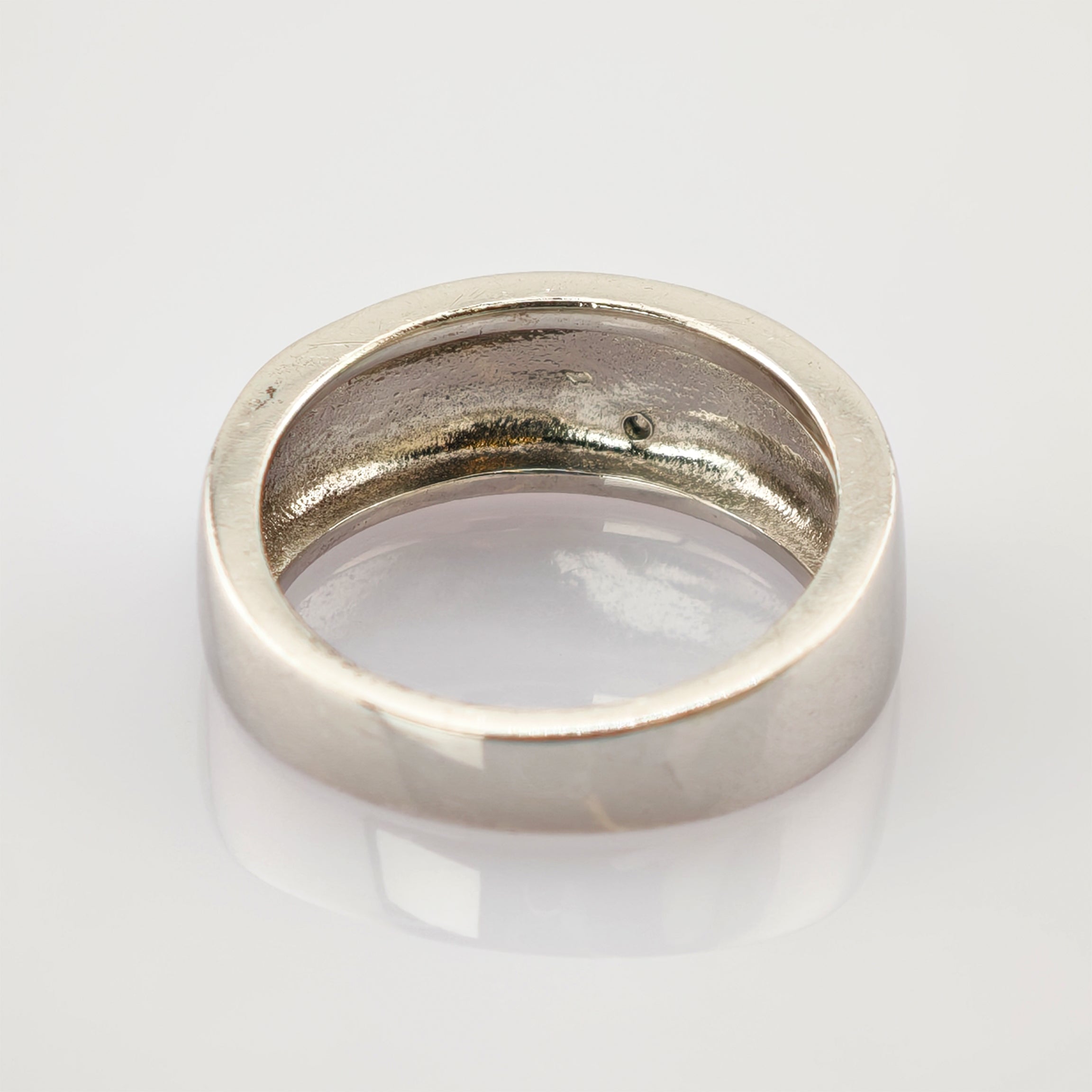 Silberner Ring mit glatter Außenseite und strukturierter Innenseite auf reflektierender Oberfläche.