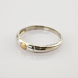 Silberner Ring mit kleinem goldfarbenem, kreisförmigem Detail auf reflektierender, weißer Oberfläche.