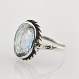 Nahaufnahme eines silbernen Rings mit ovalem, hellblauem, facettiertem Edelstein und kunstvollem Seilrand.