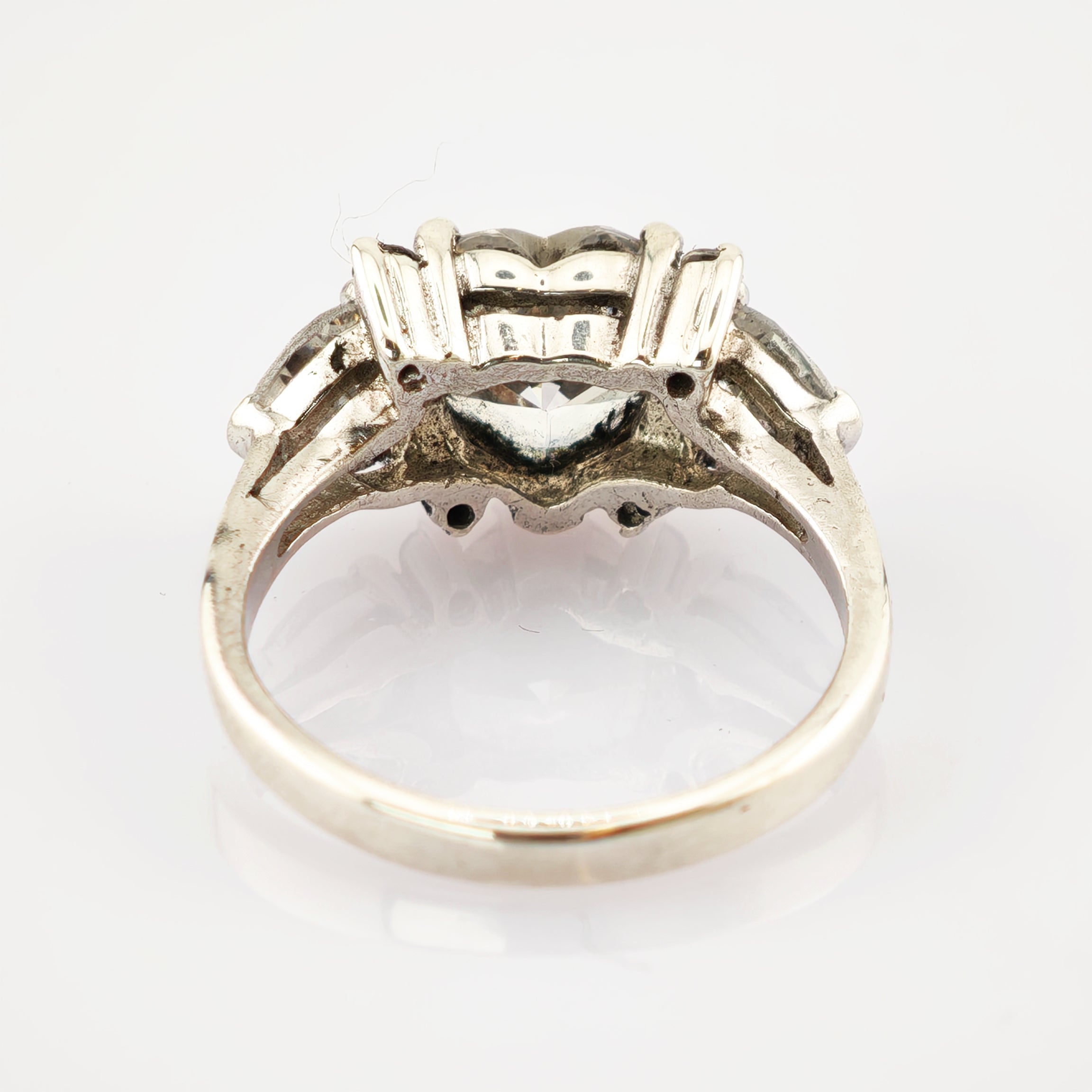 Silberner Ring mit klarem Diamant und detailliertem Metallrahmen, von hinten fotografiert.