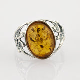 Nahaufnahme eines silbernen Rings mit ovalem bernsteinfarbenem Edelstein und organischen Details.