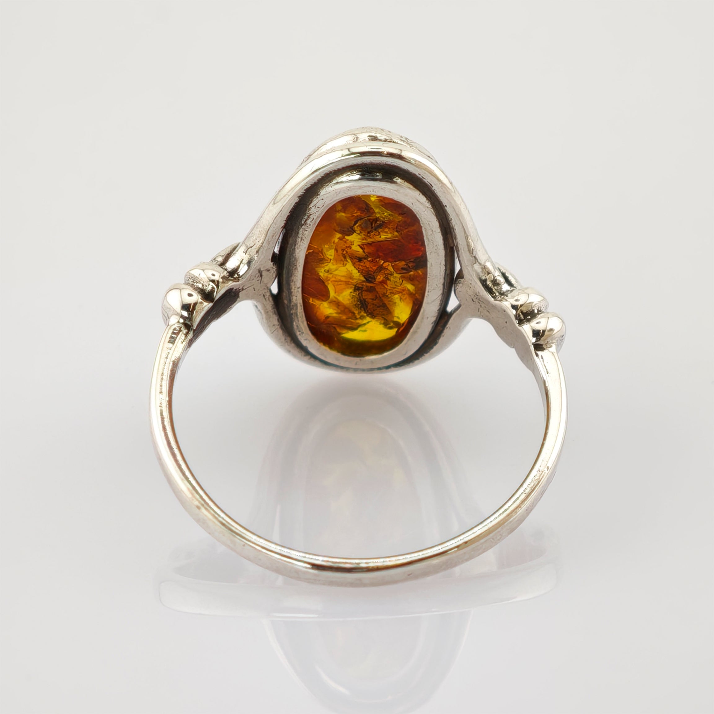 Silberner Ring mit ovalem Bernstein und filigraner Metallverzierung auf weißem Hintergrund