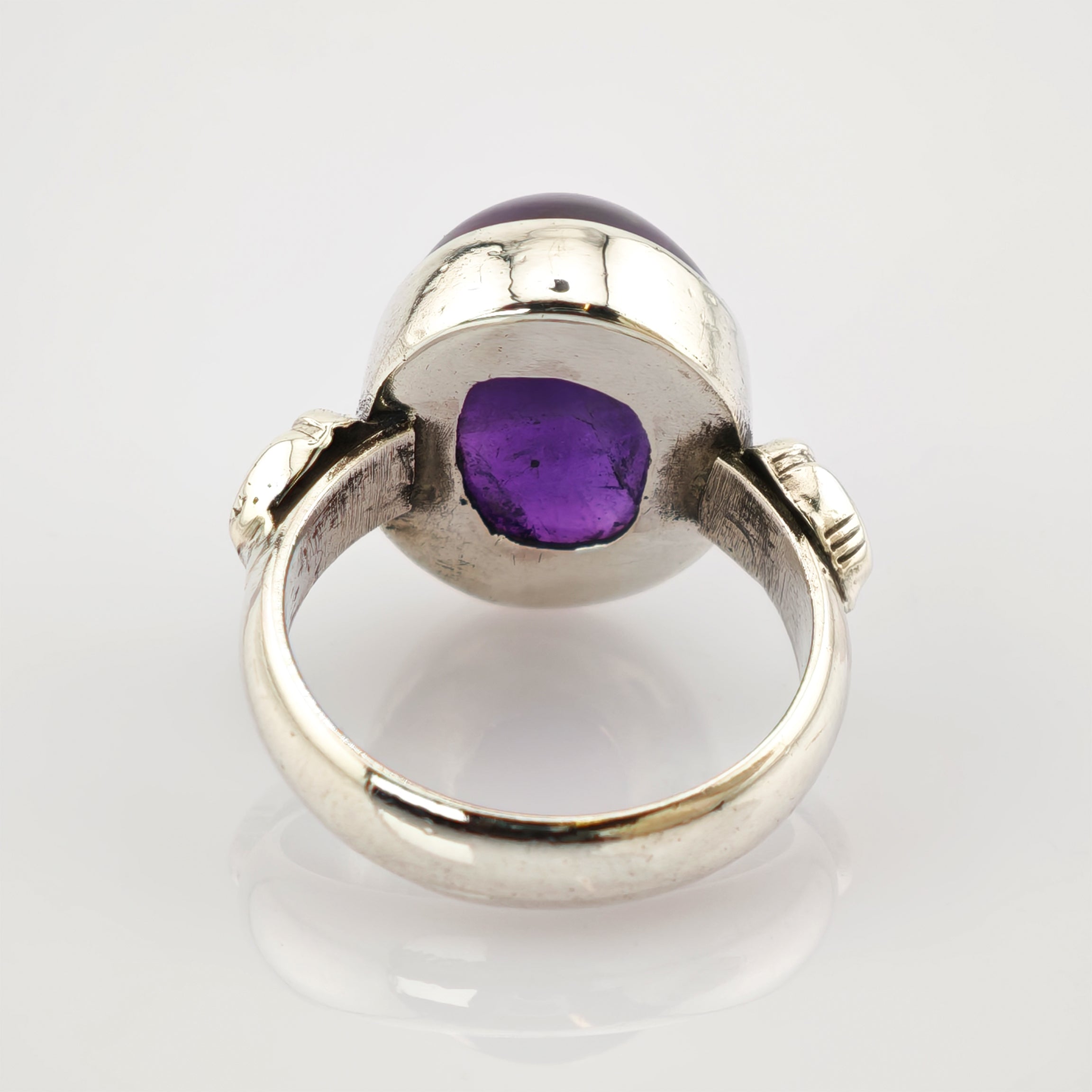 Silberner Ring mit großem ovalem violettem Edelstein und verzierten Bandseiten auf weißem Hintergrund.