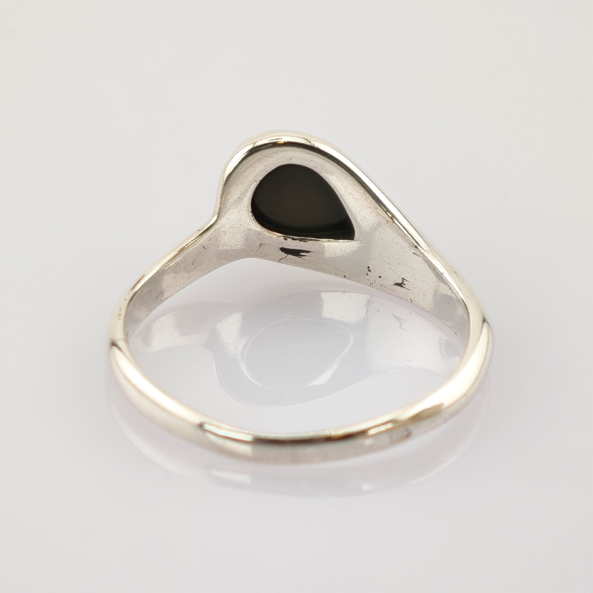 Silberner Ring mit polierter Oberfläche und schwarzer tropfenförmiger Einlage auf weißem spiegelndem Untergrund