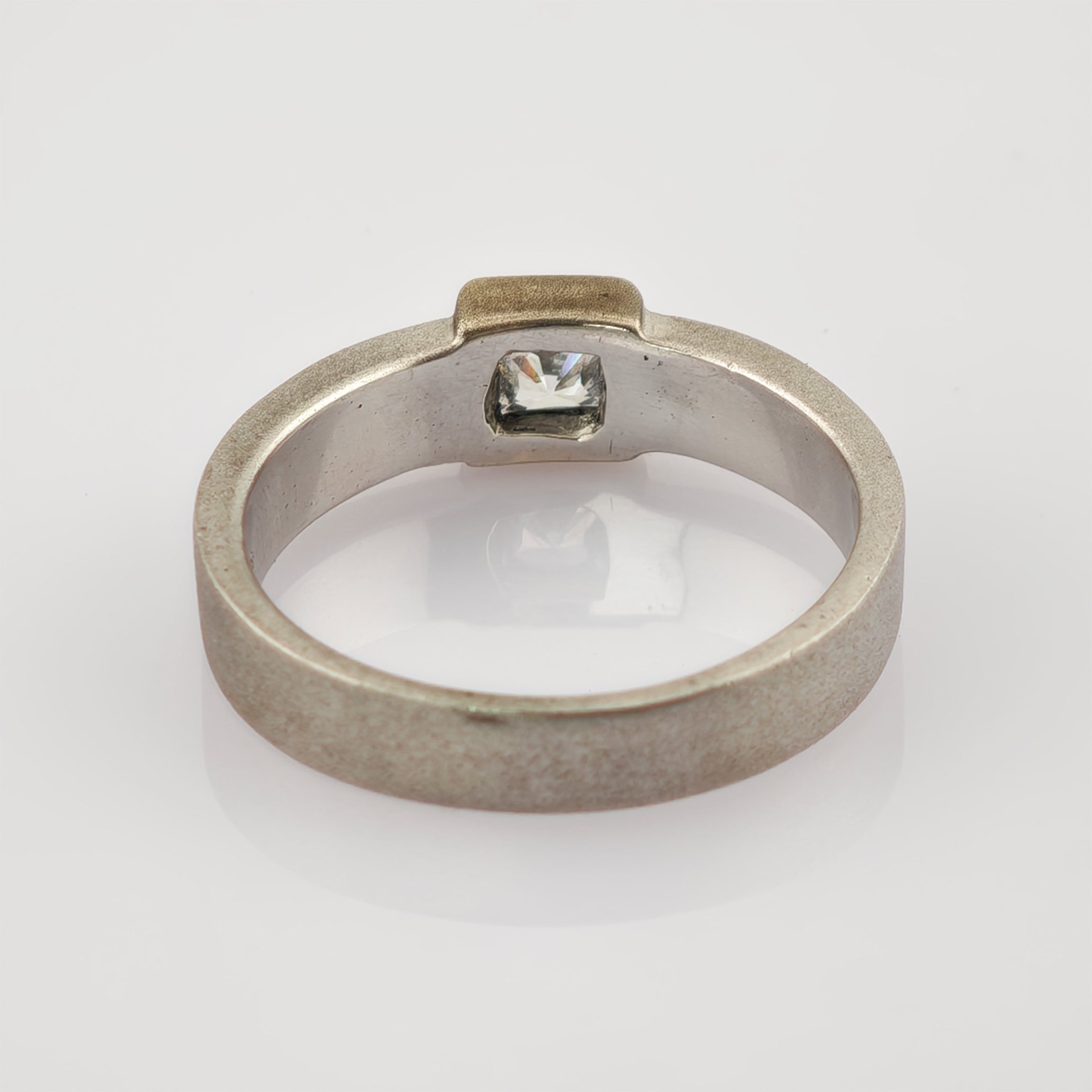 Silberner Ring mit quadratischem, klarem Edelstein und matter Oberfläche.