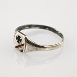 Tarnierter silberner Ring mit schildförmiger Platte, schwarzem Kreuz und rot-silbernen Streifen auf weißer Oberfläche.