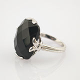 Silberner Ring mit großem, facettiertem schwarzen Edelstein und vier blattförmigen Krappen.