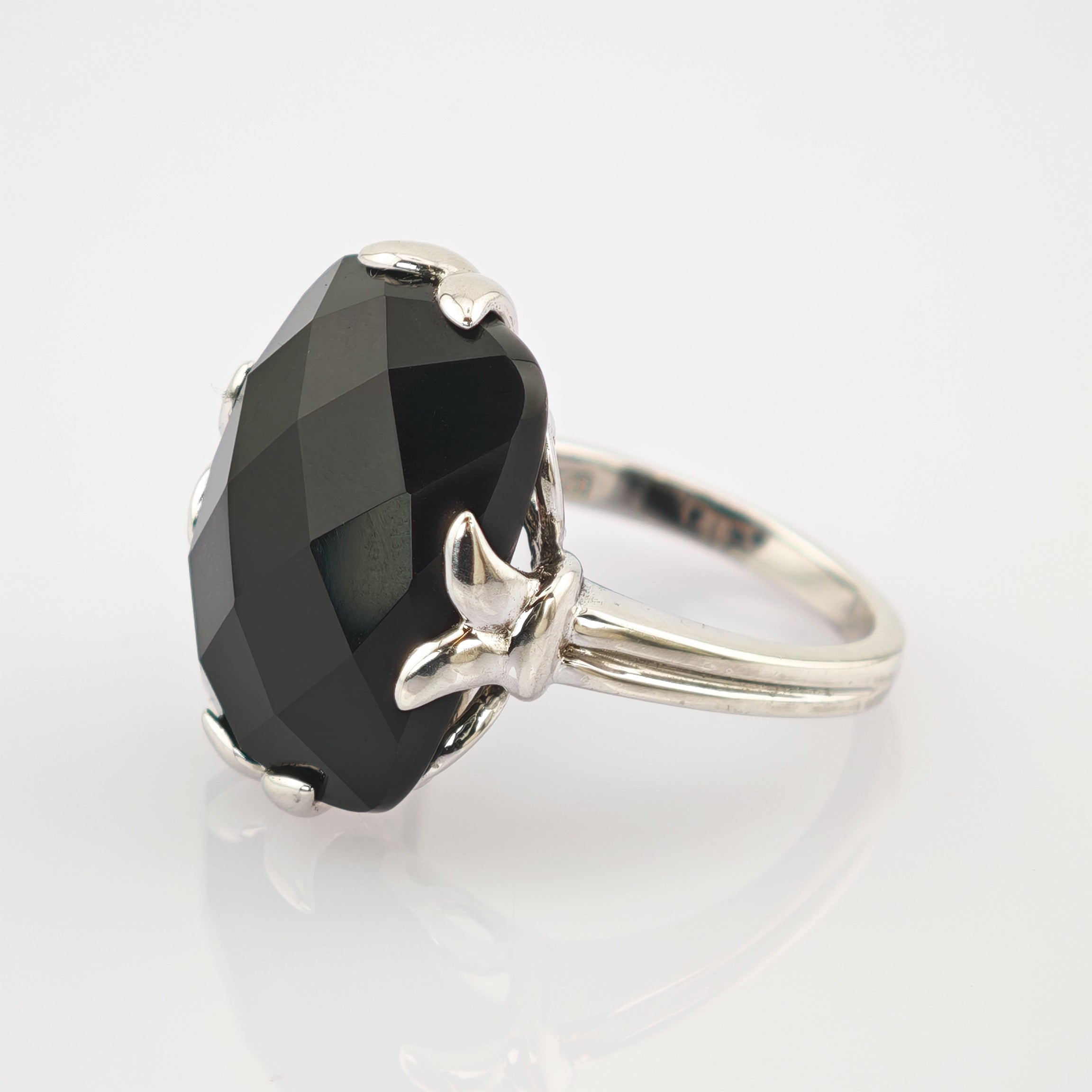 Silberner Ring mit großem, facettiertem schwarzen Edelstein und vier blattförmigen Krappen.