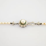 Nahaufnahme eines silbernen Schmuckverschlusses mit zentraler Perle und grünen Edelsteinen im Blumenmotiv.