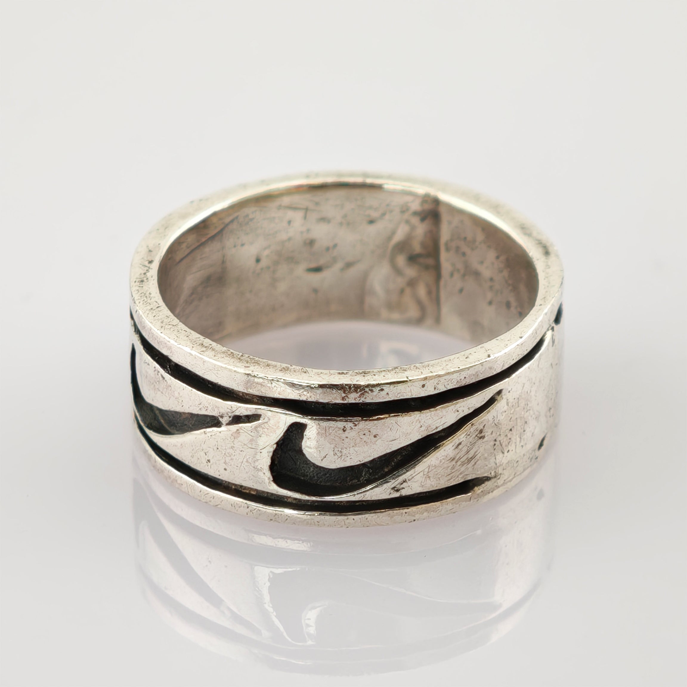 Silberner Vintage-Ring mit dunkel gefülltem Muster und Gebrauchsspuren auf reflektierender Oberfläche