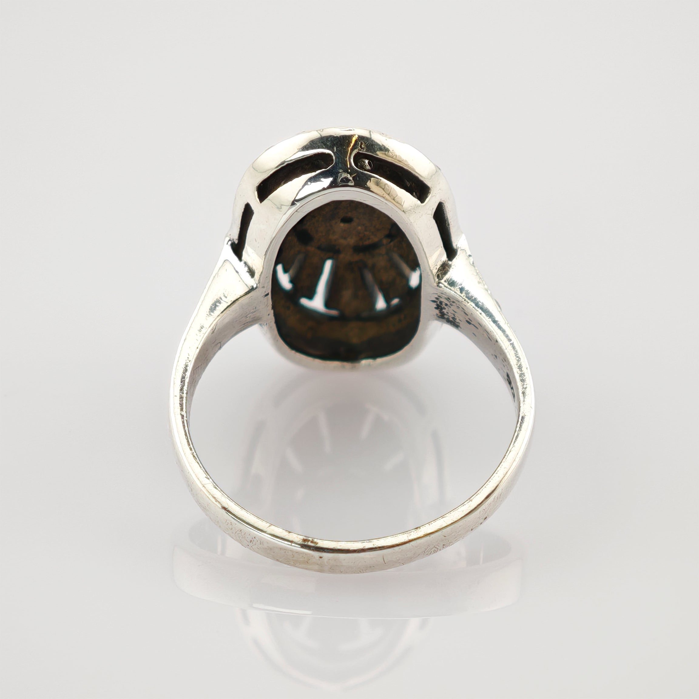 Silberner Vintage-Ring mit detaillierter hohler Fassung auf reflektierendem Hintergrund.