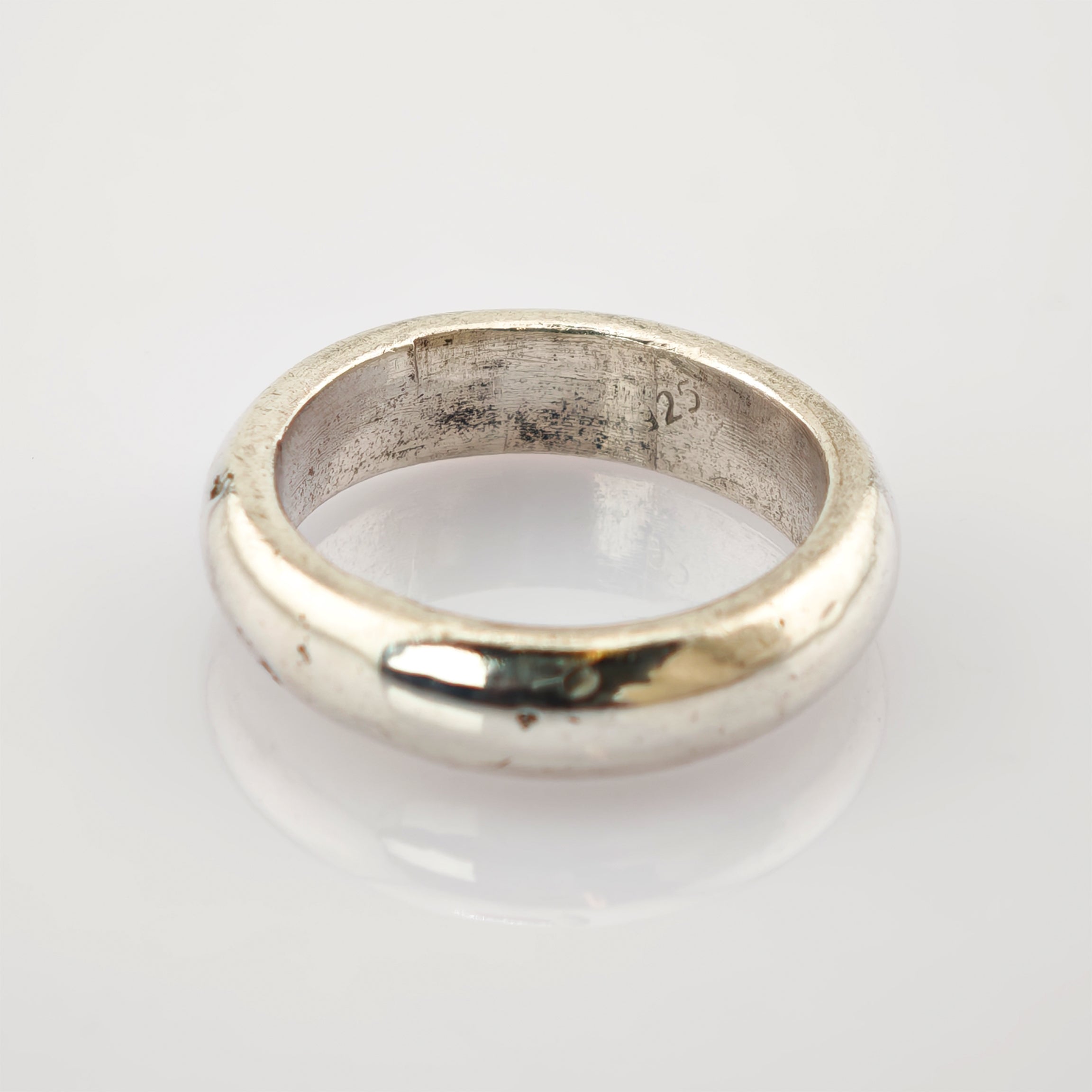 Silberner Vintage-Ring mit glatter Oberfläche und eingravierter Zahl 25 auf reflektierender Oberfläche.