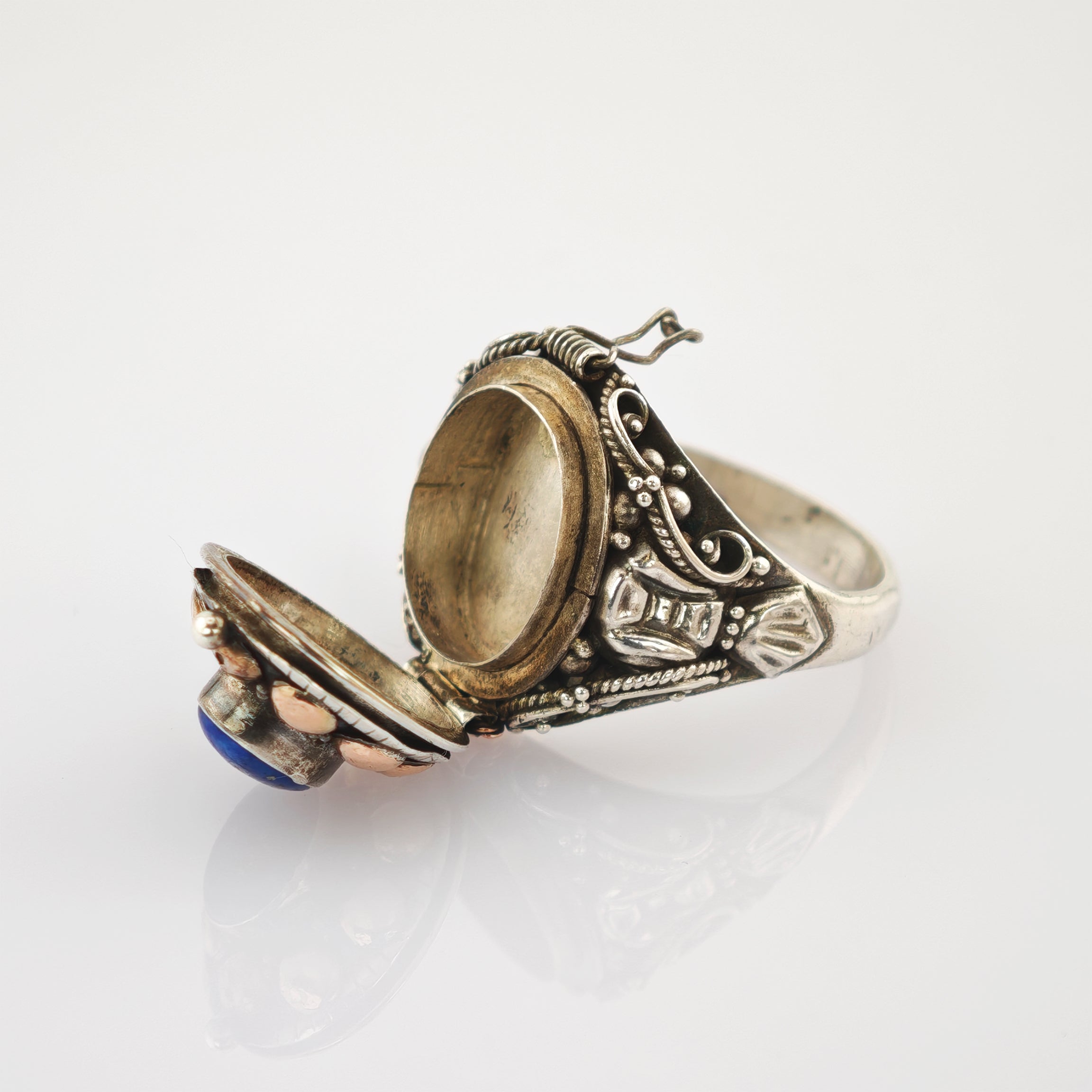 Geöffneter antiker Ring mit ovalem blauen Edelstein, umgeben von goldenen Kugeln und filigranen silbernen Verzierungen.