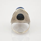 Silberring mit rundem blauem Edelstein und gedrehtem Silberseil-Design auf reflektierender Oberfläche.