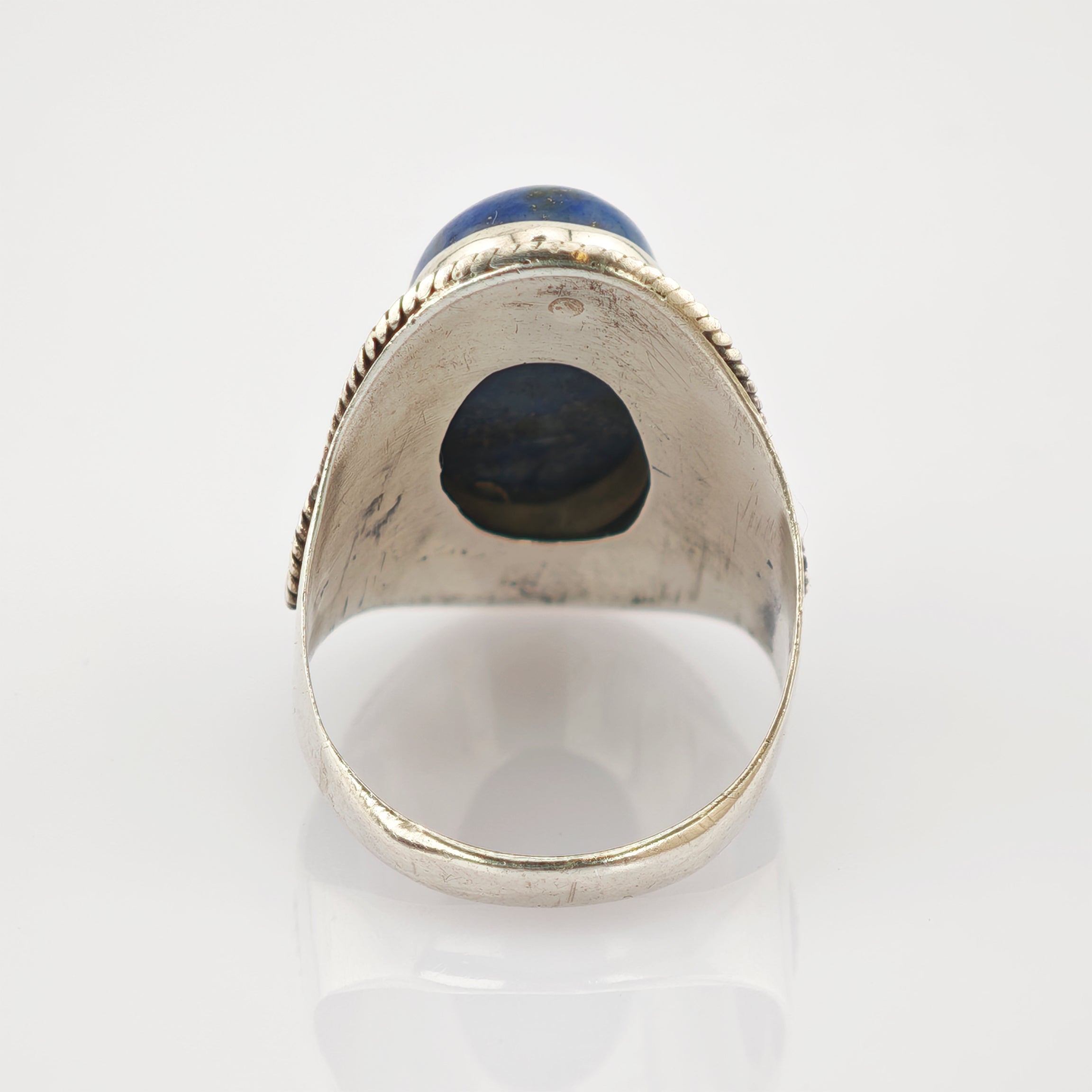 Silberring mit rundem blauem Edelstein und gedrehtem Silberseil-Design auf reflektierender Oberfläche.