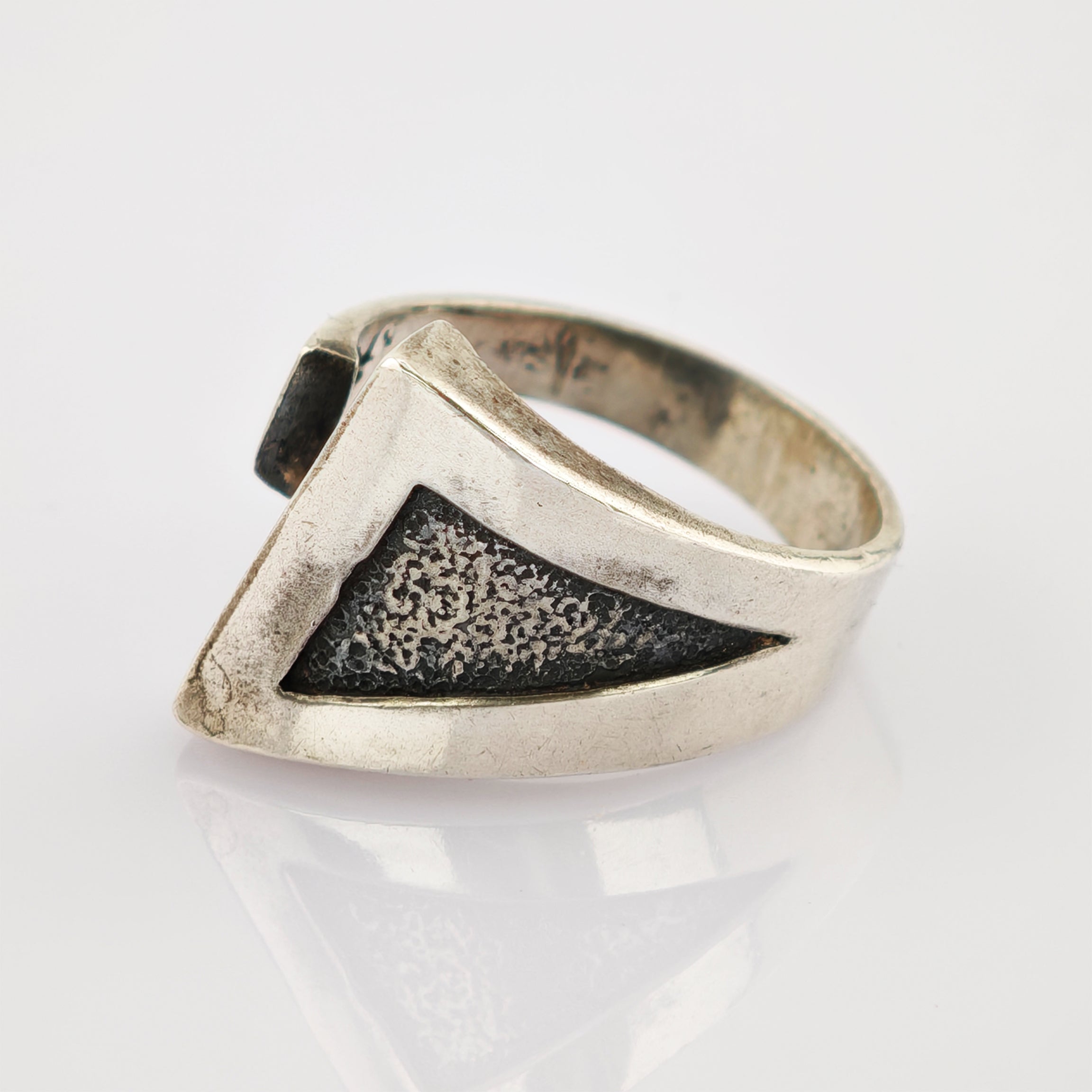 Silberring mit dreieckiger schwarzer Textureinlage auf reflektierender Oberfläche vor weißem Hintergrund.