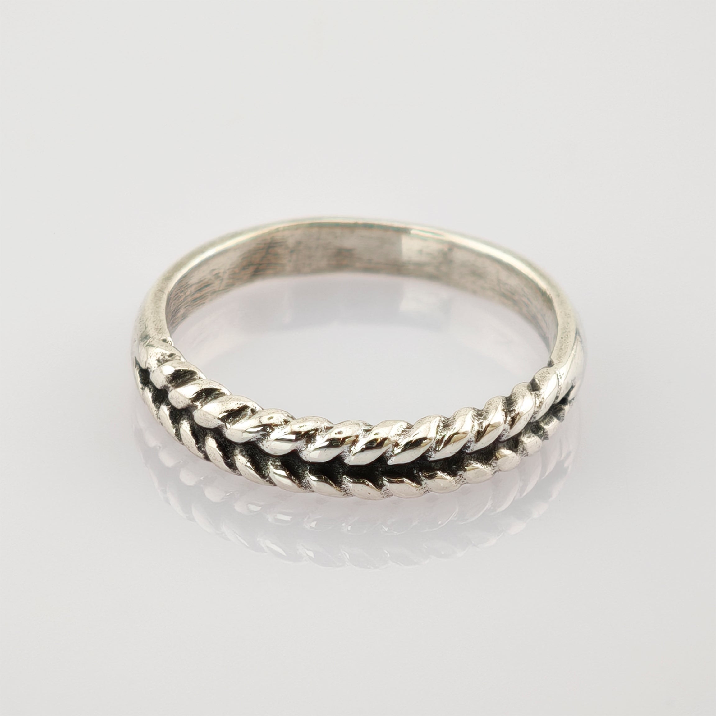 Silberring mit gedrehtem Seilmuster auf reflektierender hellgrauer Oberfläche
