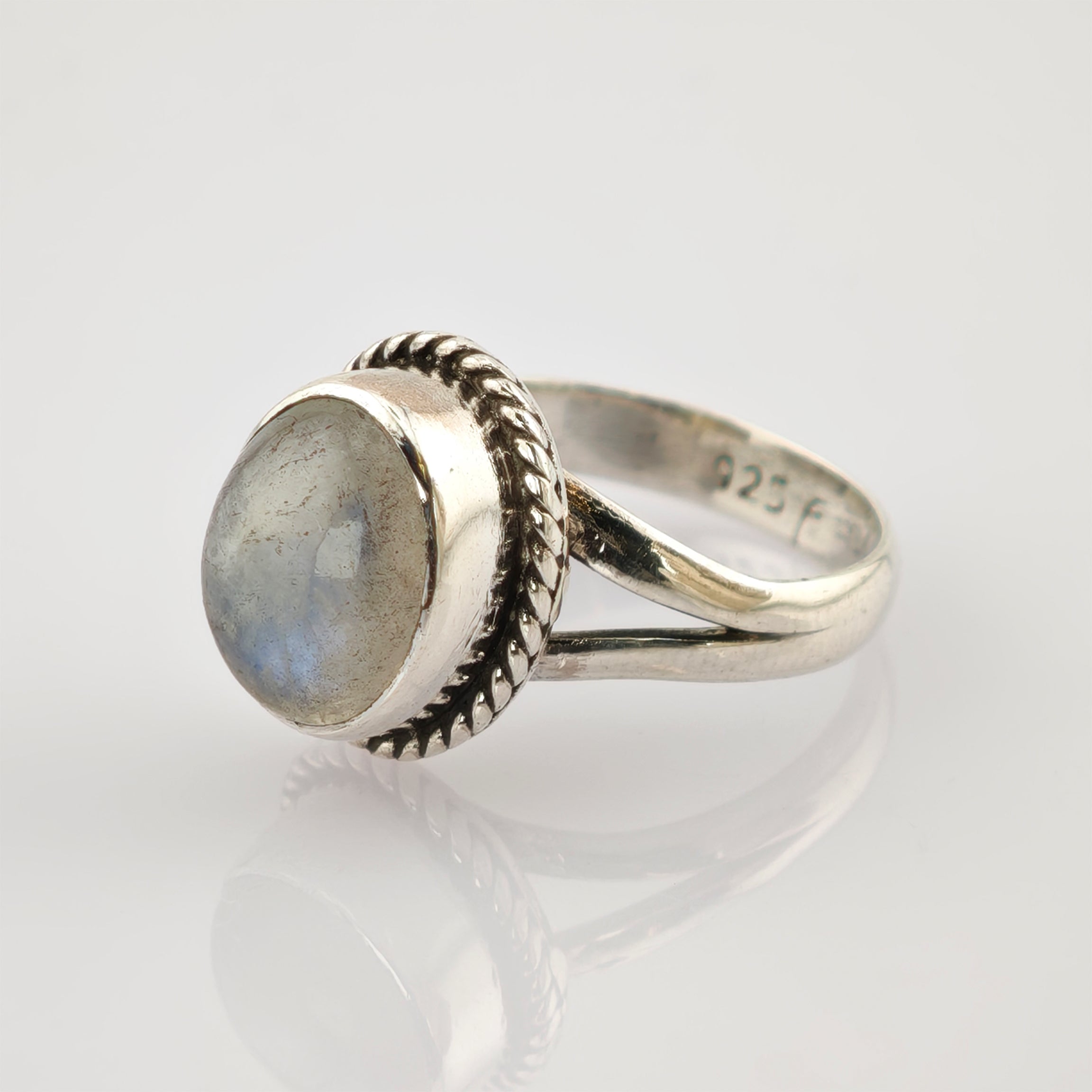 Detaillierter Silberring mit geteiltem Ringband auf reflektierender weißer Oberfläche.