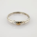 Silberring mit goldenem rundem Element in der Mitte auf reflektierender weißer Oberfläche