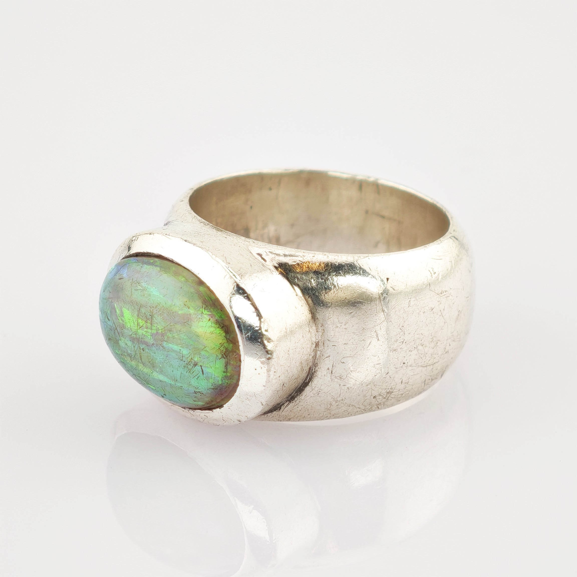 Silberring mit großem ovalem grün-blau schimmerndem Edelstein auf reflektierender weißer Oberfläche