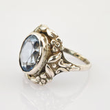 Nahaufnahme eines silberfarbenen Rings mit hellblauem ovalem Edelstein und floralen Details.