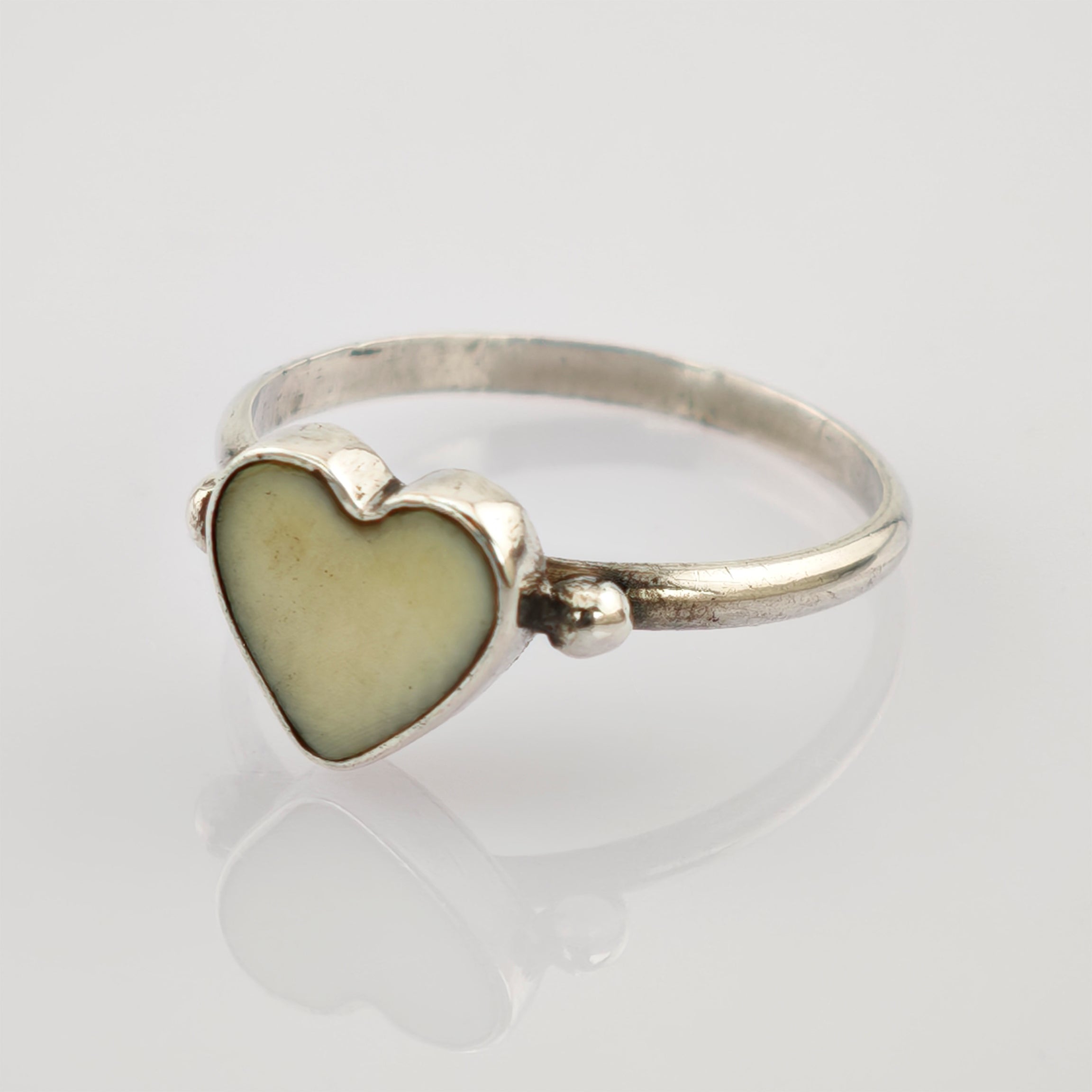 Silberring mit herzförmigem cremefarbenem Zentrum auf glänzender Oberfläche vor hellgrauem Hintergrund