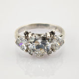 Silberring mit herzförmigem zentralem Diamanten und zwei birnenförmigen Diamanten auf reflektierendem Hintergrund