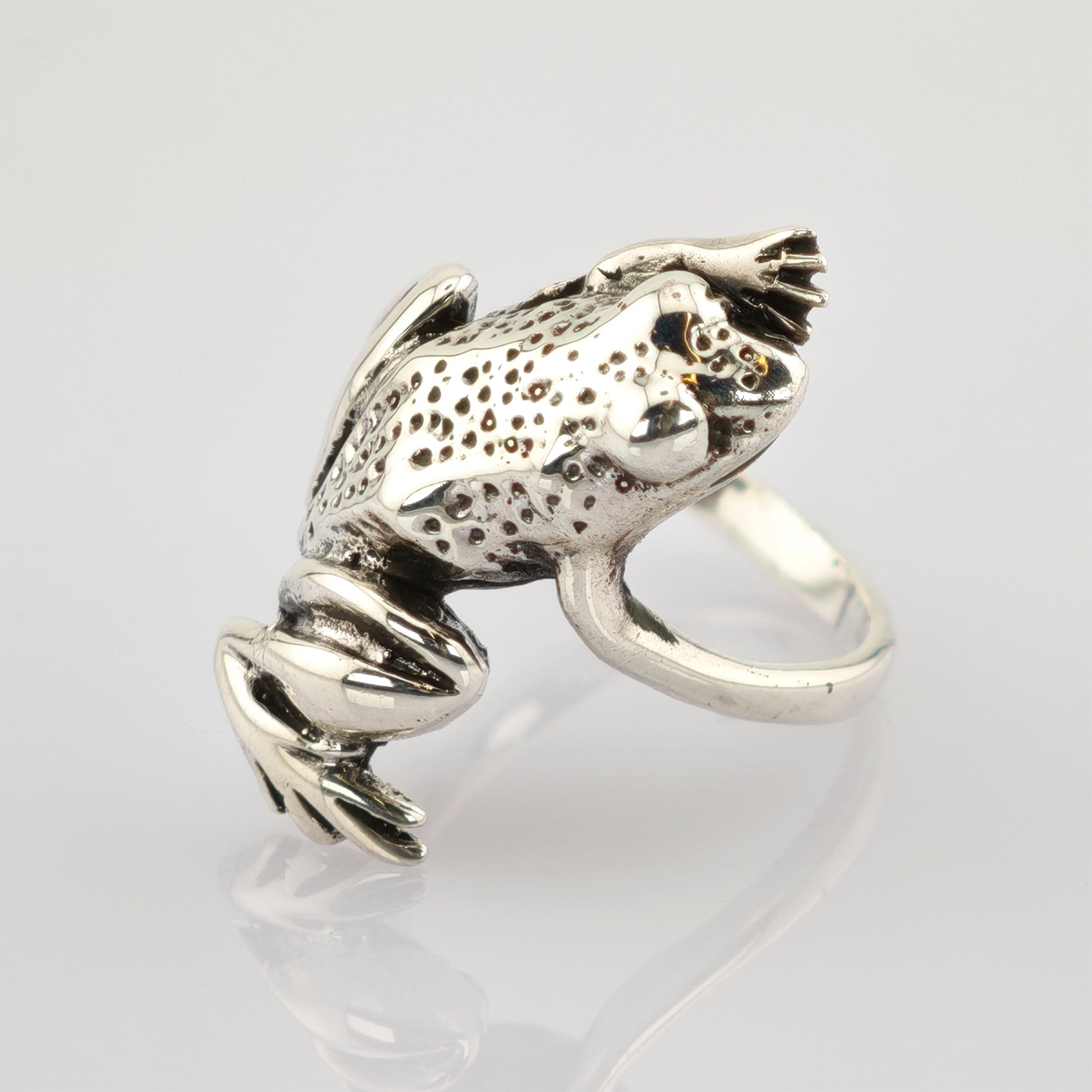 Silberring in Froschform mit texturiertem Rücken und glatten Beinen auf weißem Untergrund.
