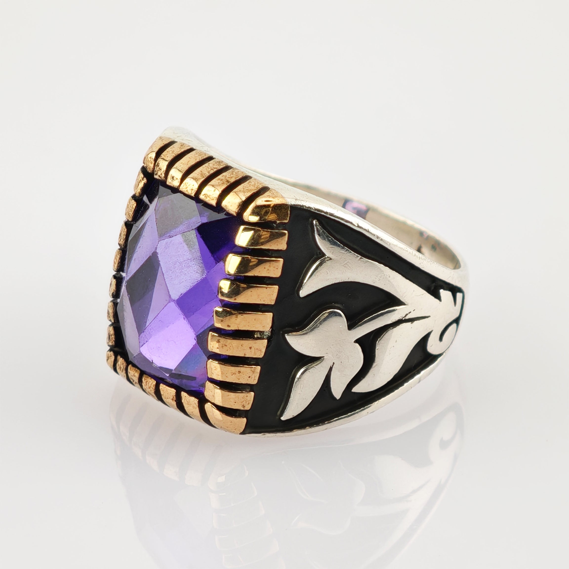 Silberring mit großem lila Edelstein und goldfarbenem Fassungsrand, verziert mit schwarzen Emaille-Floralmustern.