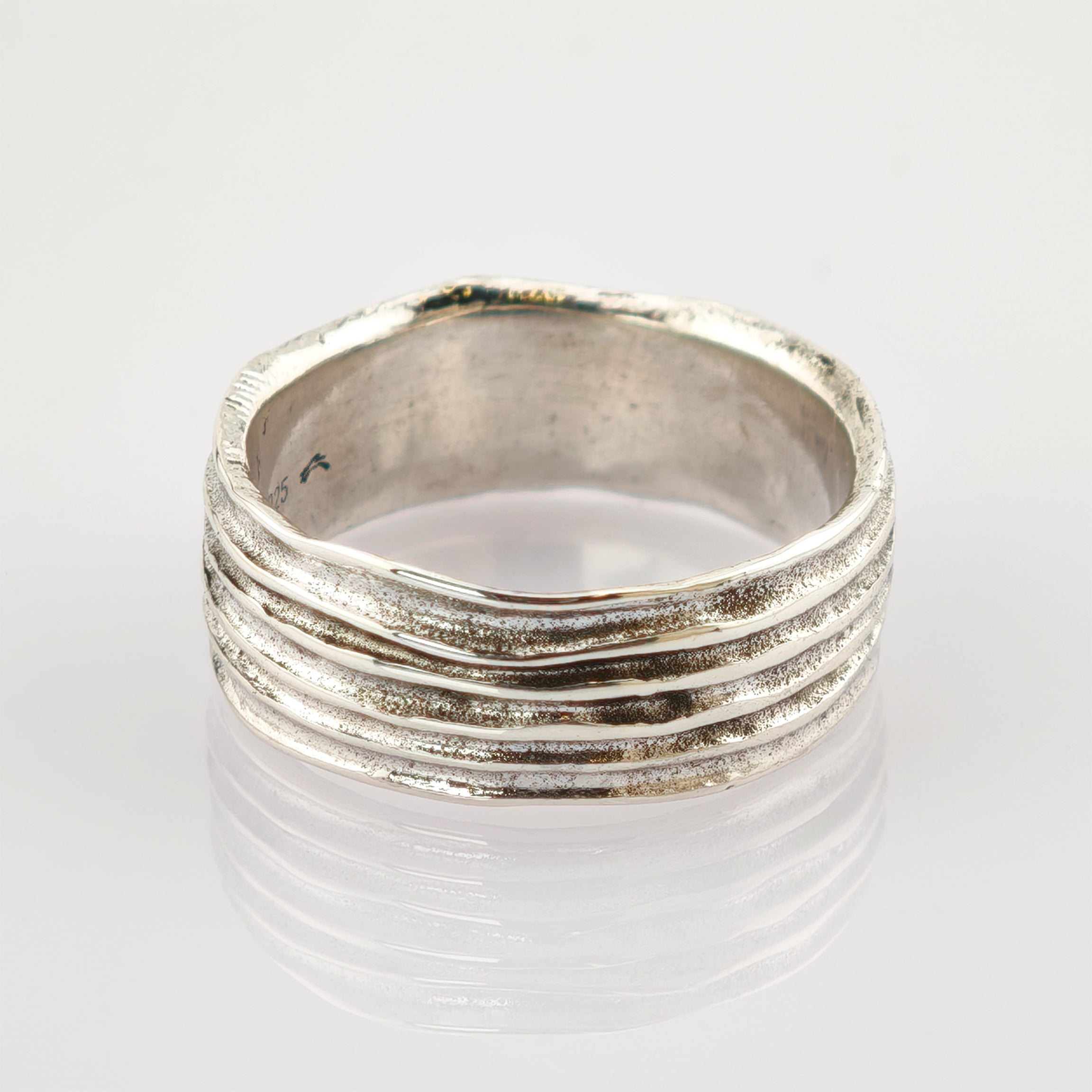 Silberring mit fünf horizontalen Erhebungen auf reflektierender weißer Oberfläche