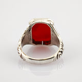 Silberring mit kunstvollen Gravuren und großem facettiertem rotem Edelstein auf weißem Hintergrund