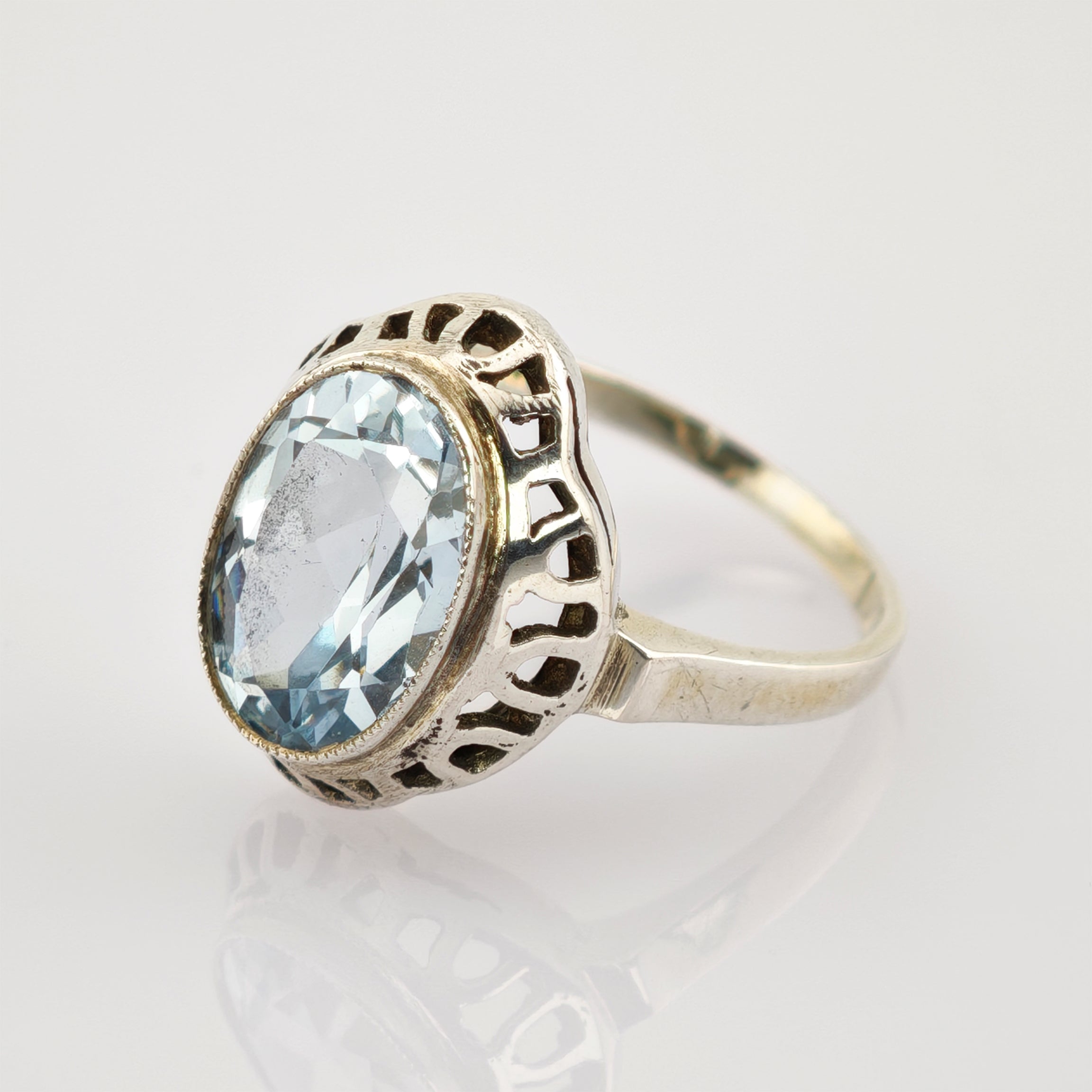 Silberring mit ovalem Aquamarin-Edelstein in offenem Chaton auf spiegelnder Oberfläche.
