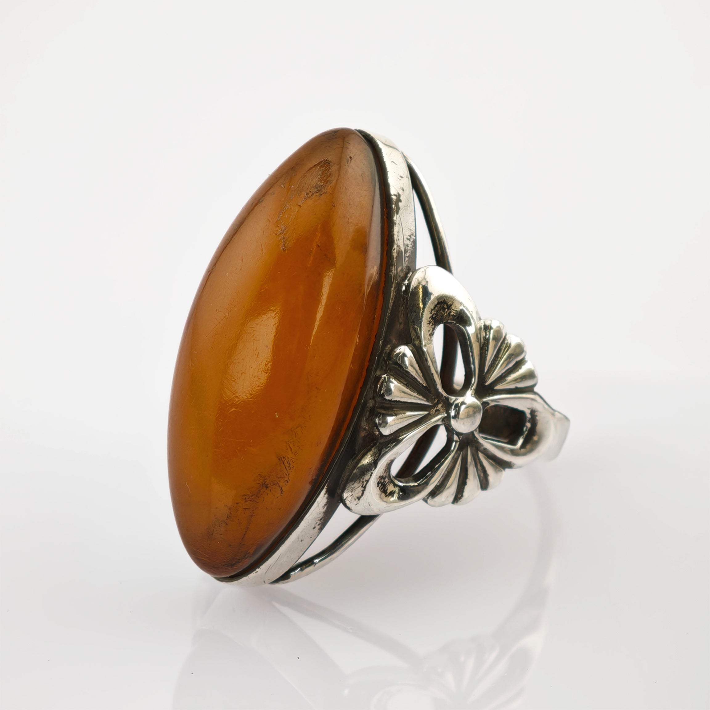 Silberring mit ovalem Bernstein und floralem Design auf weißem Hintergrund