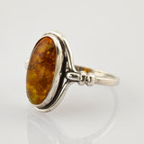 Silberring mit ovalem Bernsteinschmuck auf reflektierender Oberfläche.